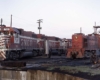 Red and white diesel locomotives next to all-red diesel locomotive beside turntable pit