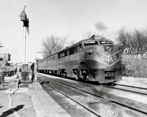 Streamlined diesel locomotive with heavyweight passenger cars at station by steam locomotive water plug