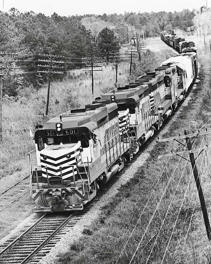Overhead view of four Gulf Mobile and Ohio diesel locomotives with freight train on S curve with multiple power lines