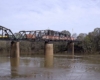 Red and white diesel locomotives with freight train on truss bridge over river