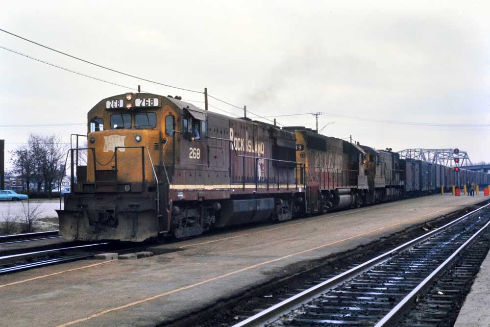 Multiple diesel locomotives with refrigerated freight cars under bridge for Rock Island perishable traffic