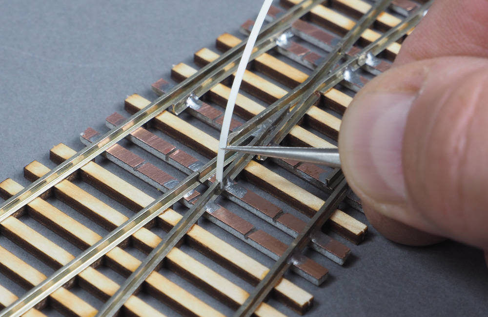  Tweezers are used to insert a strip of white styrene in a rail gap on a handmade turnout