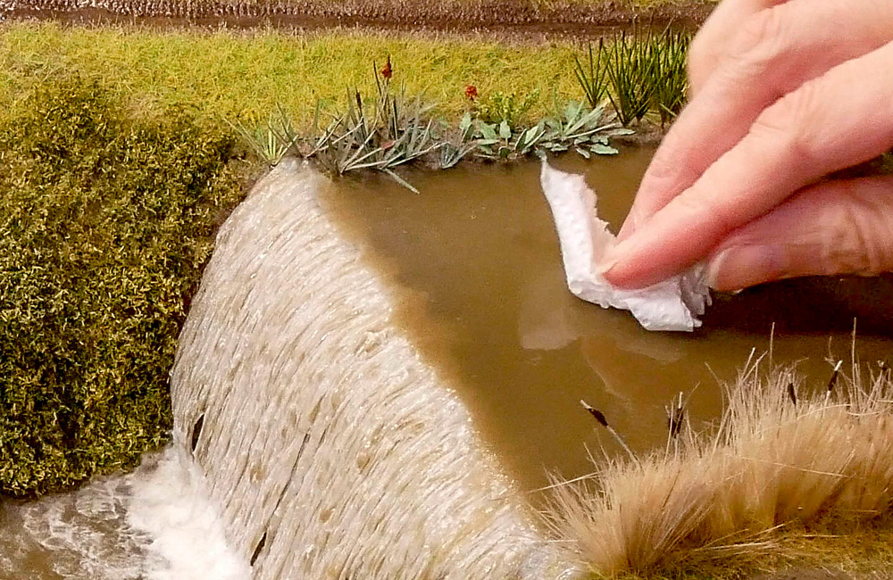 How to restore the wet water look: A scrap of paper towel is used to wipe dust from the surface of a modeled river