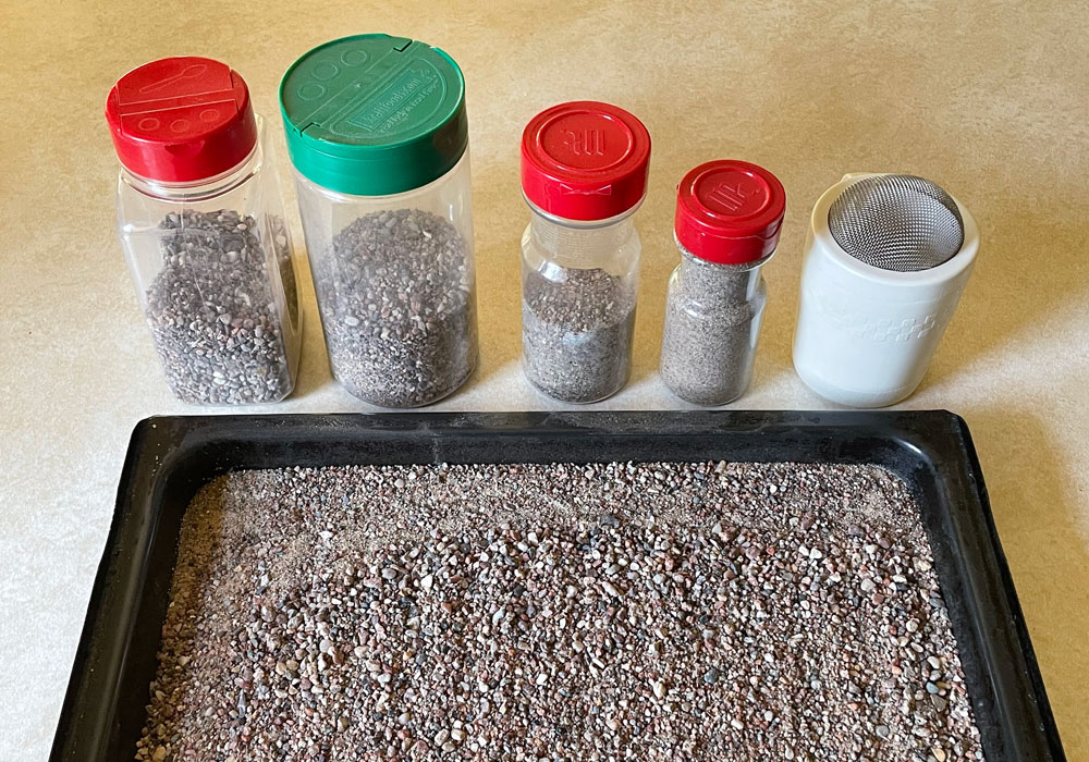 Plastic shaker bottles of gravel, grit, and sand are lined up behind a broiler tray of dirt