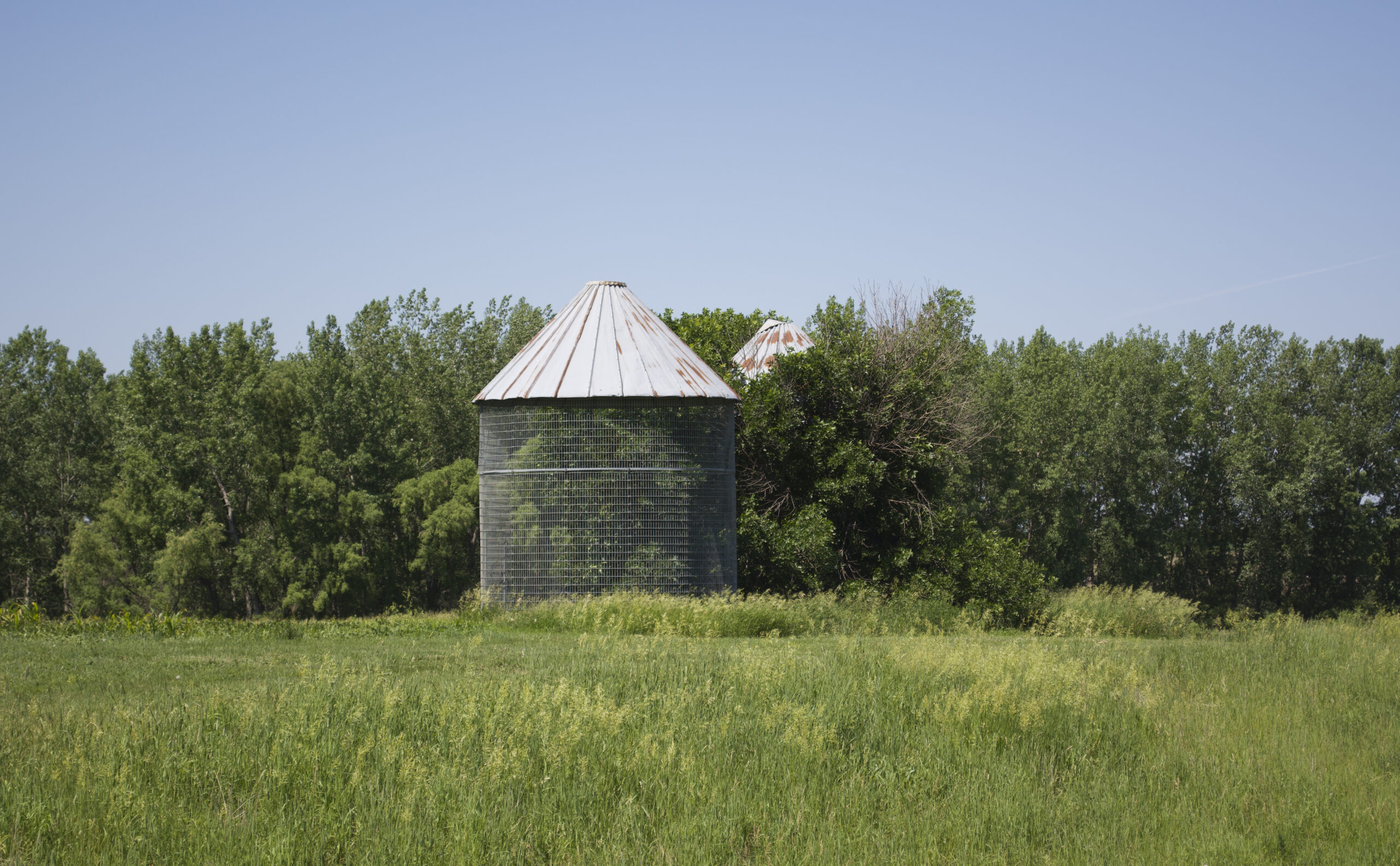 Two metal corn cribs with trees in background