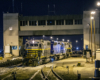 Three locomotives on a yard hump under a tower at night.