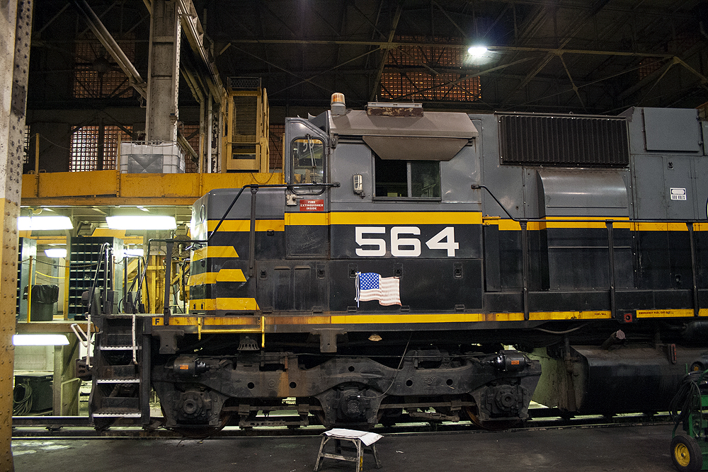 Close side-view of a black and gray diesel locomotive in a shop at night.
