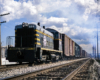 Gray and black switching locomotive leading a freight train under sunny skies with puffy clouds.