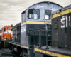 Close nose-on image of a black, yellow, and gray diesel locomotive in a rail yard.