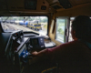 Looking over the shoulder of a locomotive engineer through a cab window at a train in a rail yard.