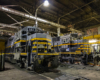 Two locomotives side-by-side in a shop at night. The locomotive on the left has a front coupler sagging.