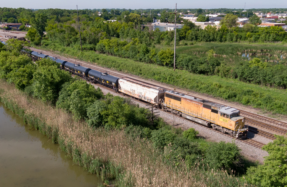 Overhead image of a yellow locomotive leading a freight train on a multi-track mainline.