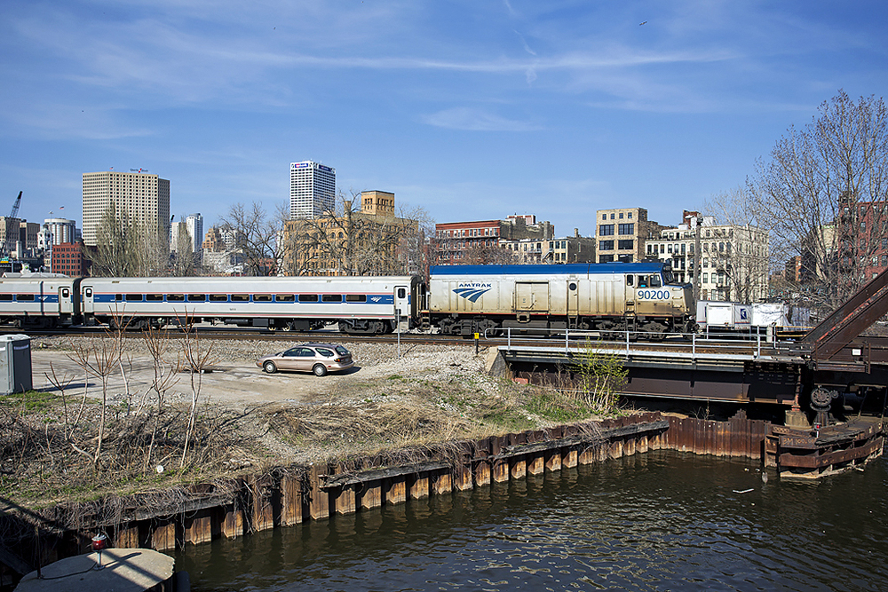 Passenger train about to pass over water on a bridge in a city landscape.