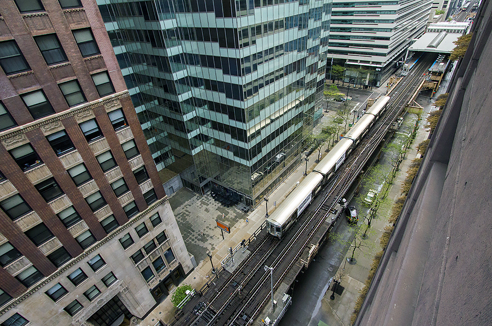 Overhead view of a train in a canyon of large buildings.