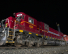 A large maroon locomotive in darkness is illuminated by photographers' lights.