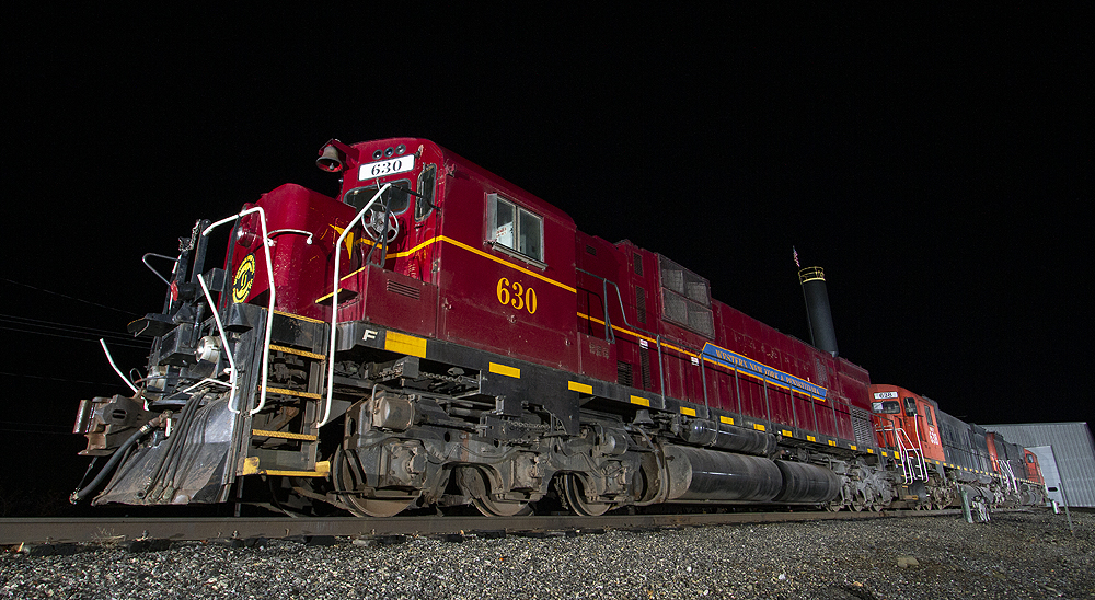 A large maroon locomotive in darkness is illuminated by photographers' lights.