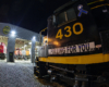 A close-up, wide-angle image of a black-and-yellow painted locomotive cab in darkness near a locomotive shop.