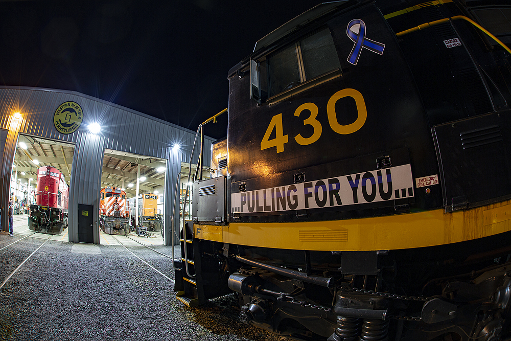A close-up, wide-angle image of a black-and-yellow painted locomotive cab in darkness near a locomotive shop.