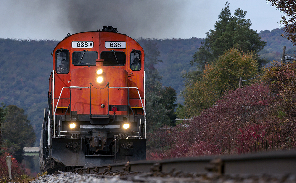 Low-angled, tight image of a red locomotive leading a train.