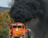 A red locomotive belches black smoke into a colorful autumnal scene.