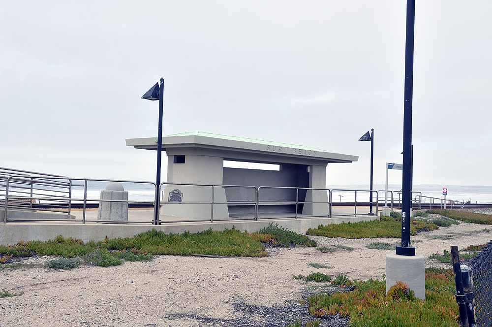 A passenger train station appears vacant on a beach under cloudy skies.