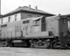 Black and white image of a locomotive near a building.