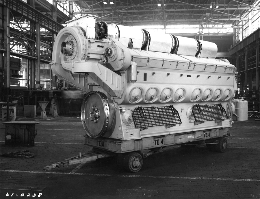 Black and white image of a large diesel engine on a shop floor, on a heafty cart.