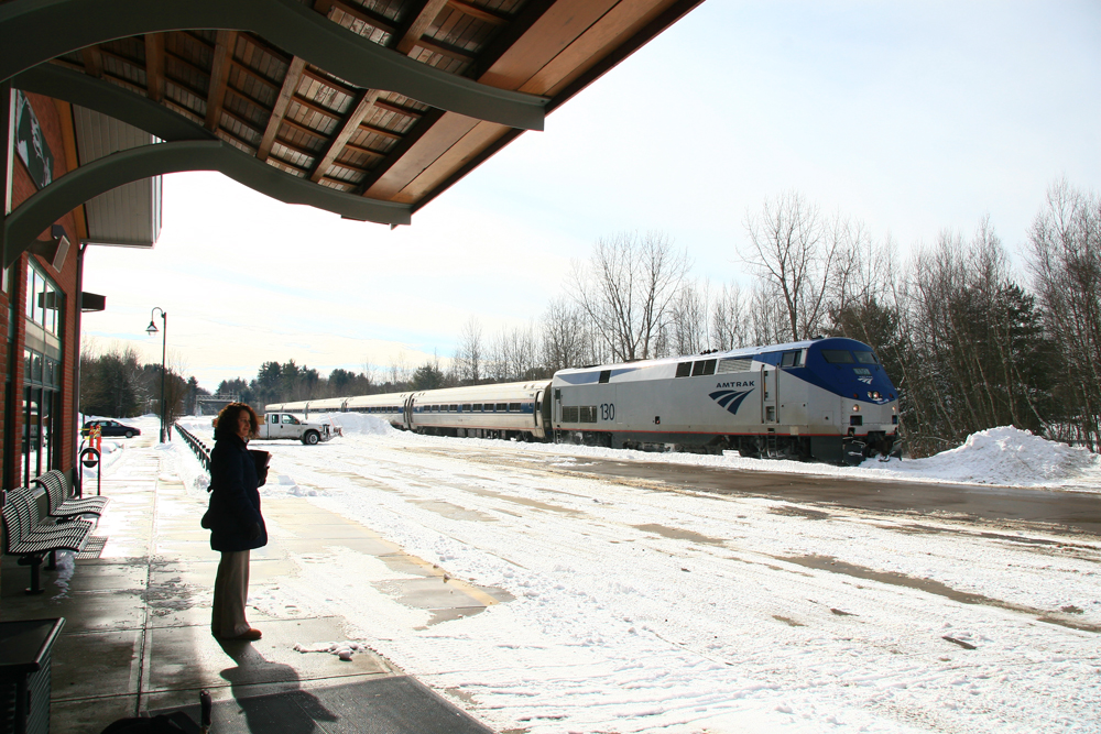 Woman waits on snow-covered platform as passenger train arrives