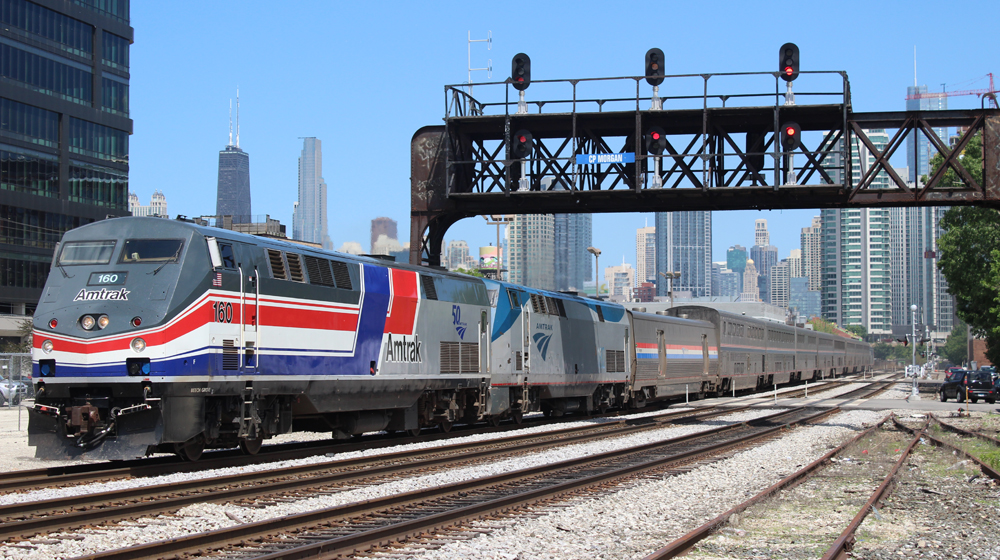 Passenger train led by locomotive in heritage red, white, and blue striped scheme.