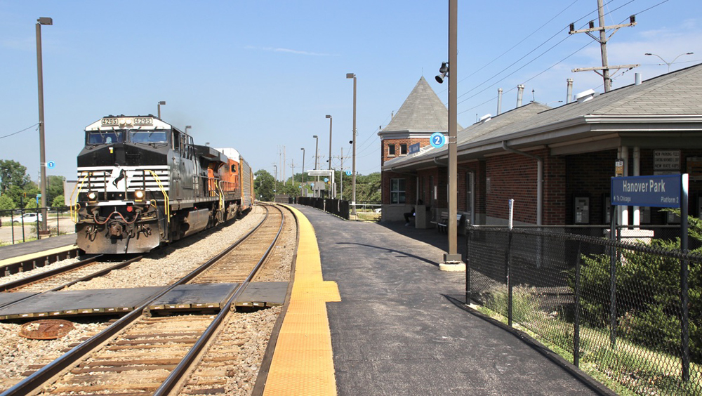 Freight train with black locomotive passes commuter rail station