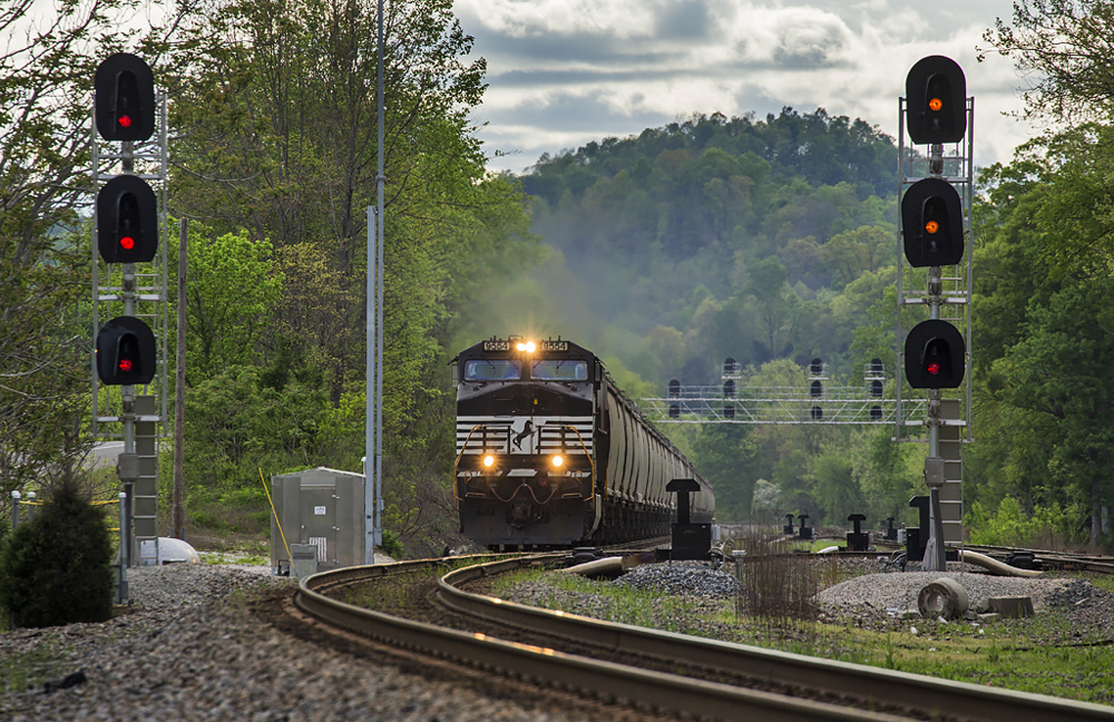 Train of hopper cars led by black locomotive approaches curve in mountains