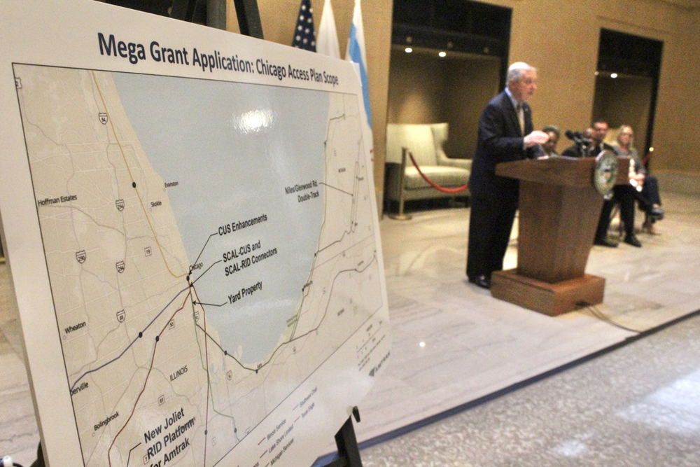 Poster with map in foreground as man speaks at podium