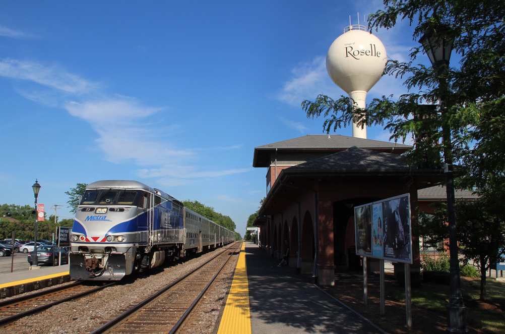 Commuter train arrives at station; water tower with name Roselle is in the background