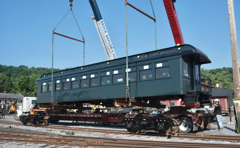 Dark green passenger car body is lifted off of transport truck