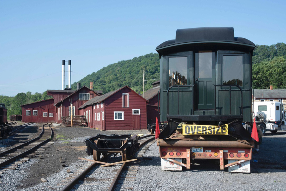 End view of dark green passenger car on truck trailer with wheelsets on adjacent track