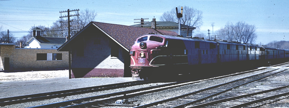 1960s passenger train with three locomotives passes station