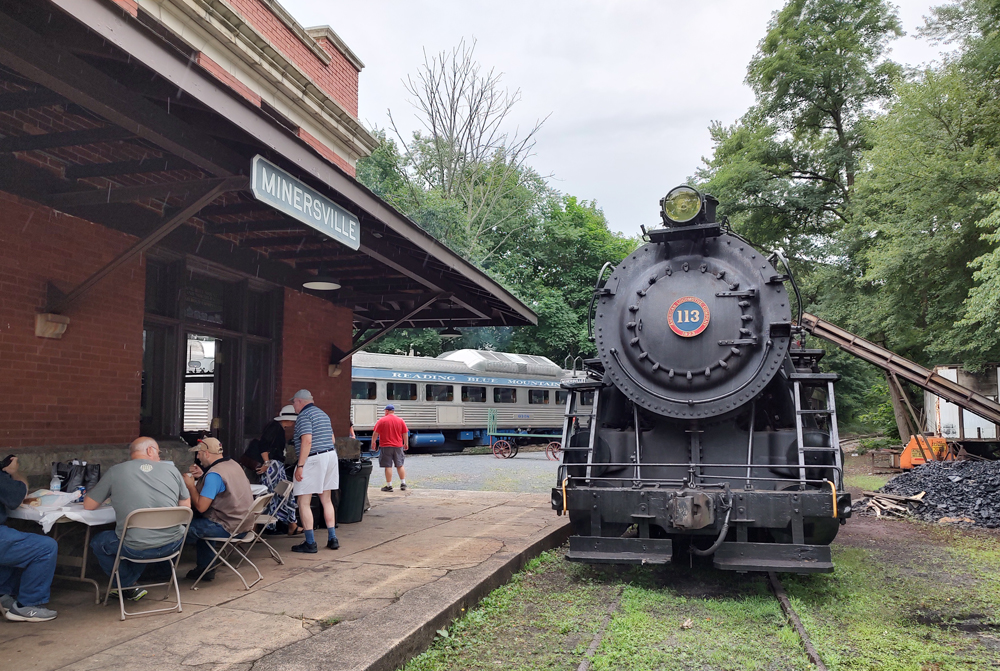 Men eating at table on station platform next to steam locomotive