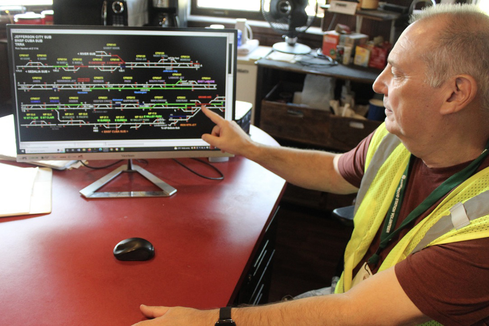 Man in yellow safety vest points at track diagram on computer screen