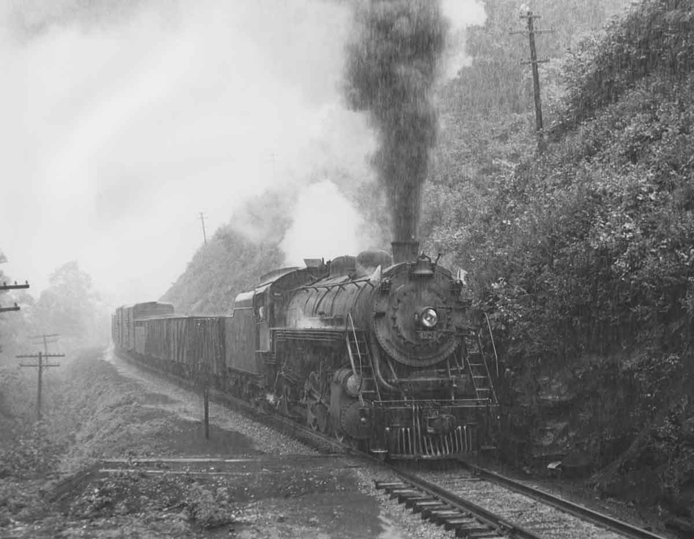 Steam locomotive climbing hill in rainstorm