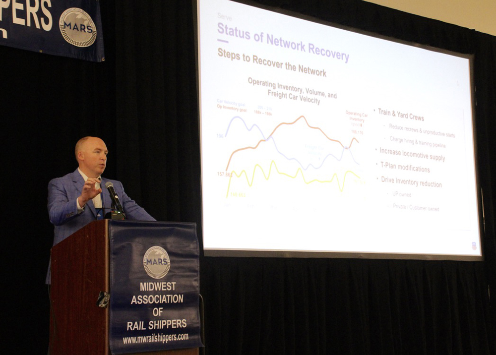 Man speaking at podium, with chart projected on screen next to him