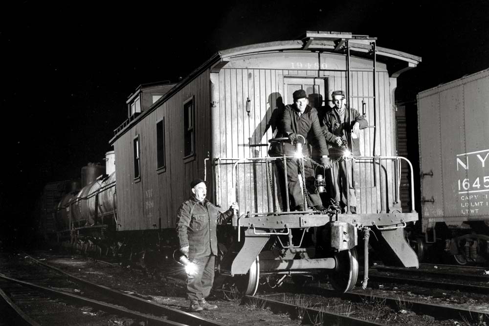 Men stand on wooden caboose at night