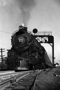 Steam-powered passenger train under signal bridge