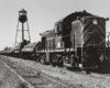 Diesel locomotive with log train in front of water tower