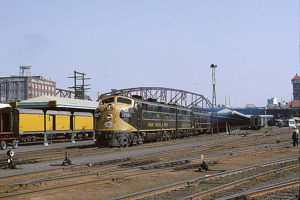 Streamlined yellow and green Spokane, Portland and Seattle Railway diesel locomotives with passenger train in station under bridge