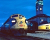 Streamlined diesel locomotive by station with clock tower at dusk