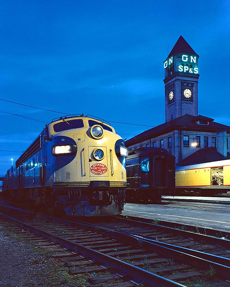 Streamlined diesel locomotive by station with clock tower at dusk