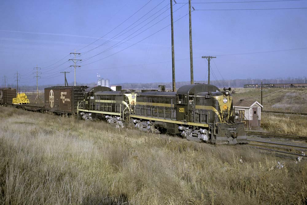 Green-and-yellow diesel locomotives with freight train in yard
