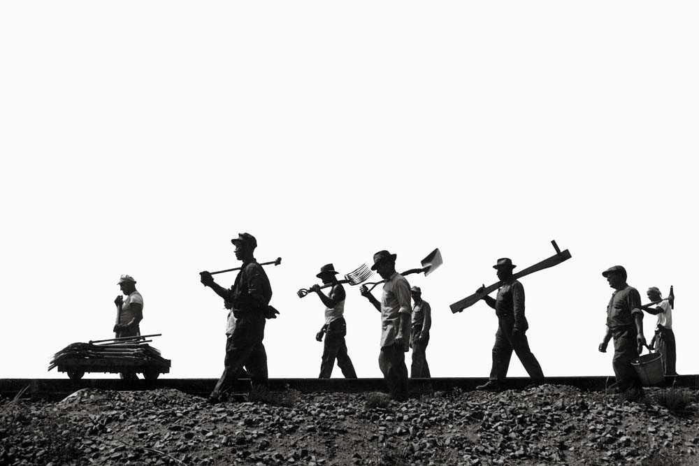 Men walk with tools along railroad tracks