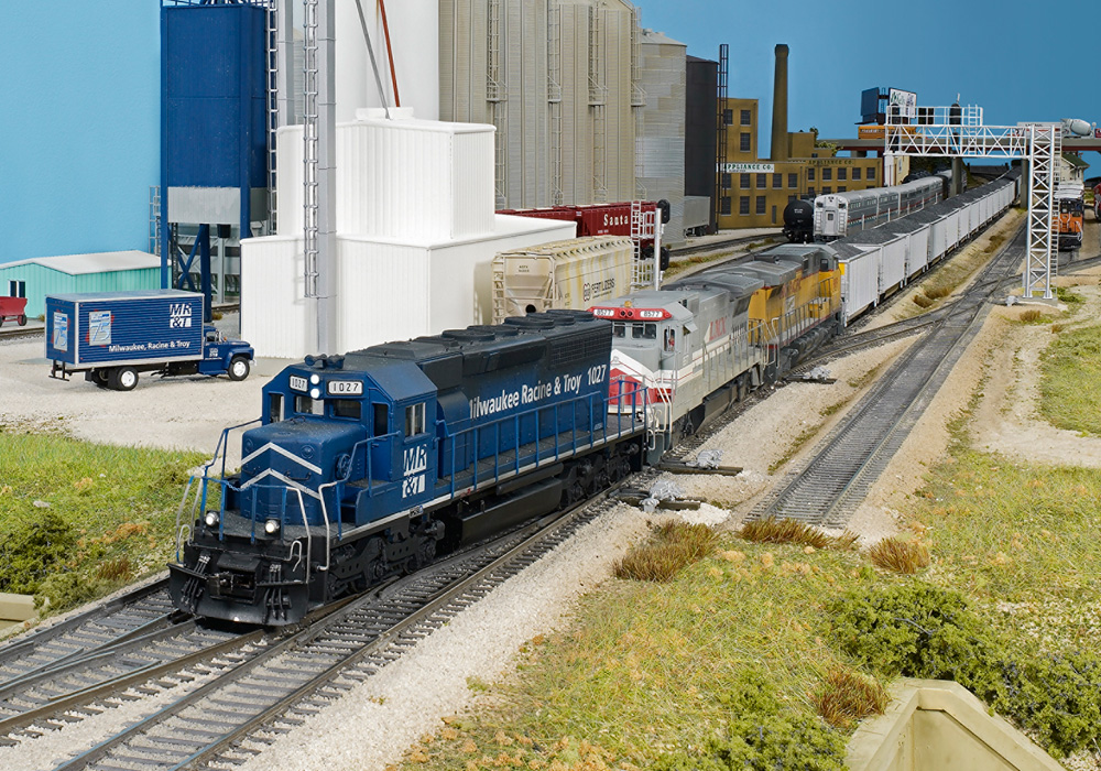 A trio of diesel locomotive models pulls a coal train on an HO scale model railroad layout.