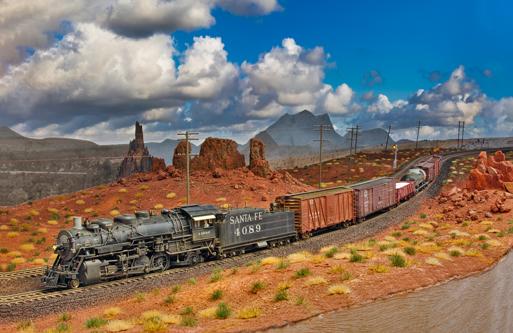 An Atchison, Topeka & Santa Fe 2-8-2 Mikado steam locomotive pulls a short freight through a Southwestern desert landscape